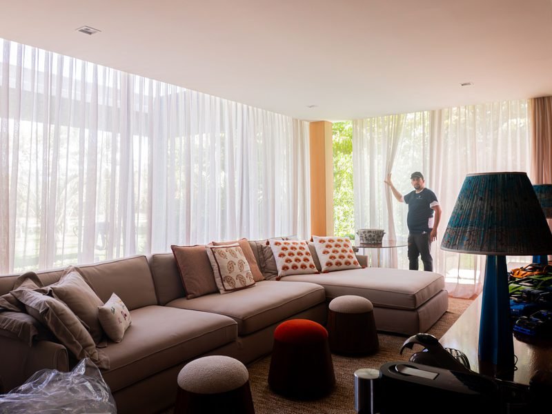 Profissional da Prime Cortinas ajustando a cortina de voil de uma sala ampla, depois da higienização
