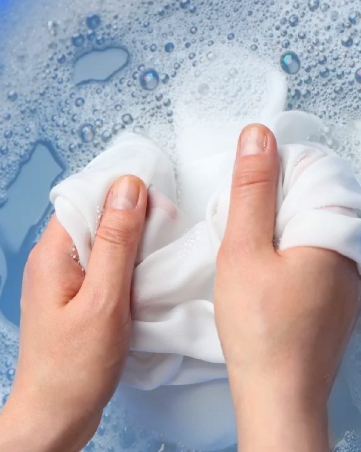 Mãos lavando uma cortina de voil branca à mão, dentro da água com espuma